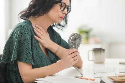 A woman blowing the fan at herself to cope with hot flashes. © Getty Images 